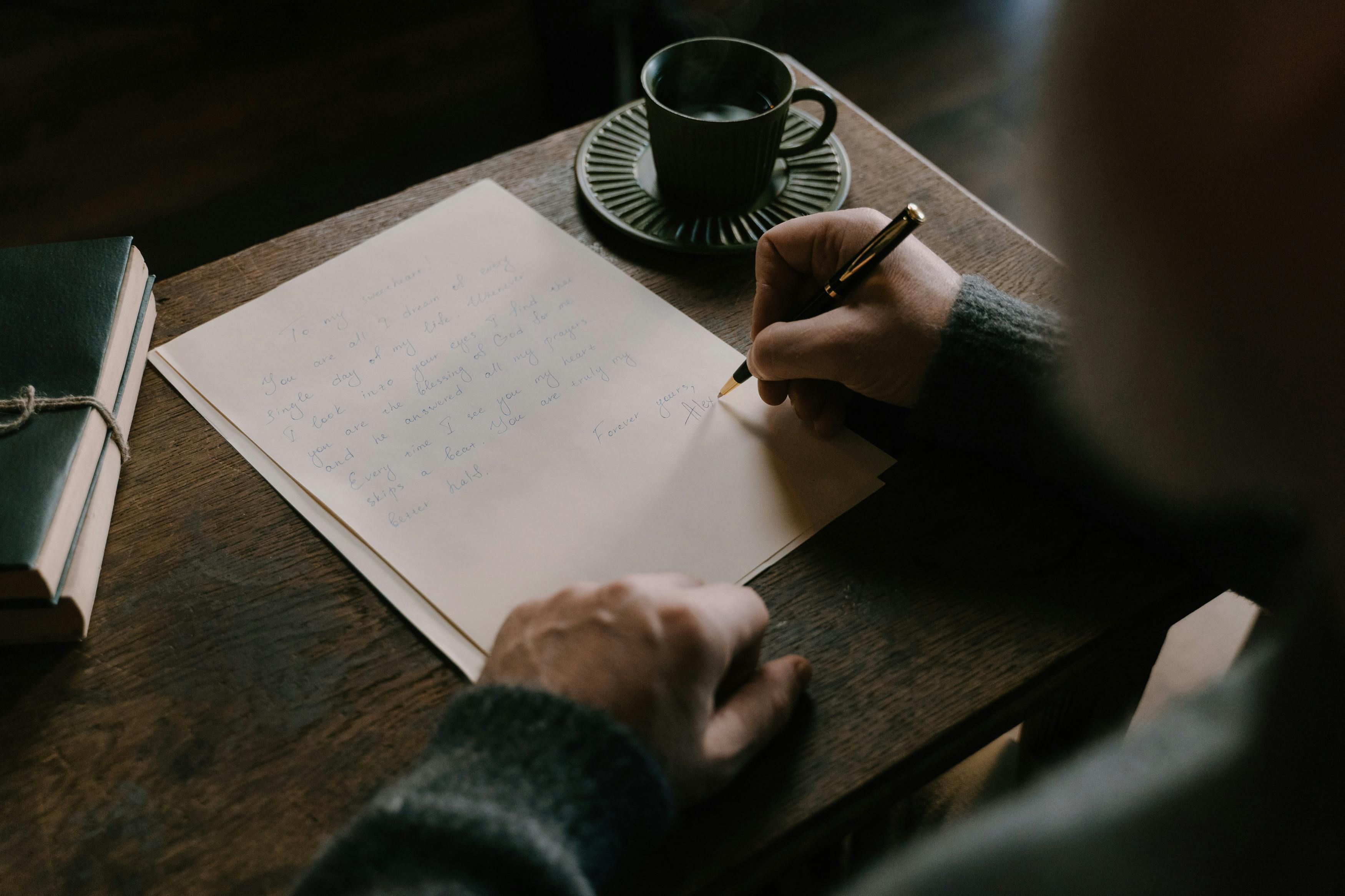 A pair of hands writing a letter on lined paper, viewed from above. Top-down composition, warm natural light.
